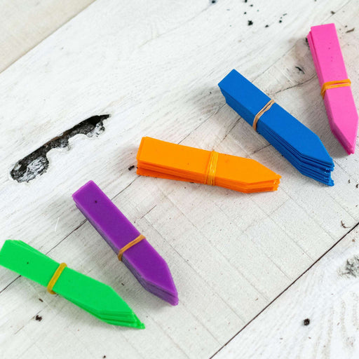 Bundles of colorful plastic garden plant markers (blue, pink, orange, purple, green) on rustic white wood.