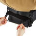 Hands fastening a black Velcro strap on a tan and black outdoor gear bag, showing adjustable buckles for secure closure.