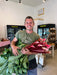 Smiling farmer holds fresh red rhubarb and leafy greens at a farm market. Local produce, farm-to-table.