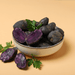 Bowl of dark-skinned purple potatoes, some sliced to reveal vibrant purple flesh. Fresh parsley garnish. Healthy vegetables.
