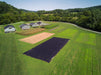 Agricultural research farm aerial: greenhouses, corn, diverse crop plots, prepared beds, and weed barrier, surrounded by forests.
