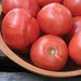 Vibrant red tomatoes, freshly picked, piled in a light wooden bowl on a dark rustic background.
