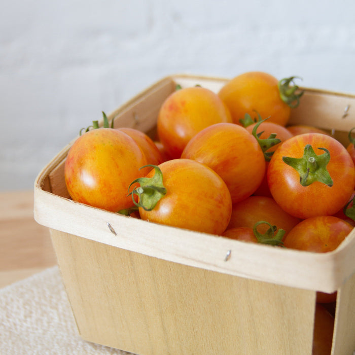 Ripe orange and yellow striped cherry tomatoes with green stems, packed in a wooden farmers market basket.