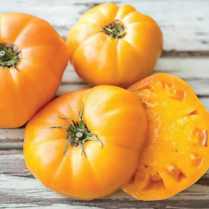 Vibrant, ripe orange heirloom tomatoes, whole and sliced, on a rustic wooden surface.