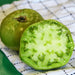 Fresh green tomatoes, one whole and one cut in half, showcasing the vibrant flesh and seeds on a white checkered cloth.