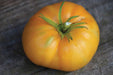 Vibrant yellow heirloom tomato with green stem on rustic wood. Fresh, ripe garden produce, perfect for eating.