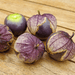 Purple tomatillos on wood, some with partial papery husks. One exposed, revealing purple fruit and green crown. Fresh for salsa.
