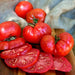Fresh, ripe red heirloom tomatoes, whole and sliced, glistening with water droplets on a wooden cutting board.