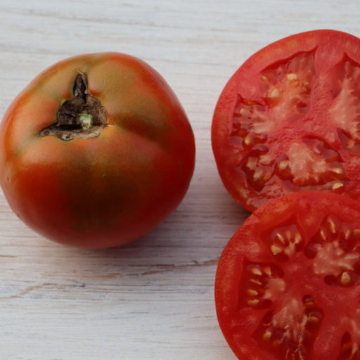 Fresh, ripe red tomato and two sliced halves displaying juicy pulp and seeds on a light wood background.