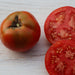 Fresh, ripe red tomato and two sliced halves displaying juicy pulp and seeds on a light wood background.