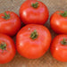 Six ripe red tomatoes with green calyxes on a woven mat. Fresh organic produce, garden vegetables.