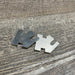 Two silver notched metal shims on grey wood grain. Precision spacers for mechanical alignment.