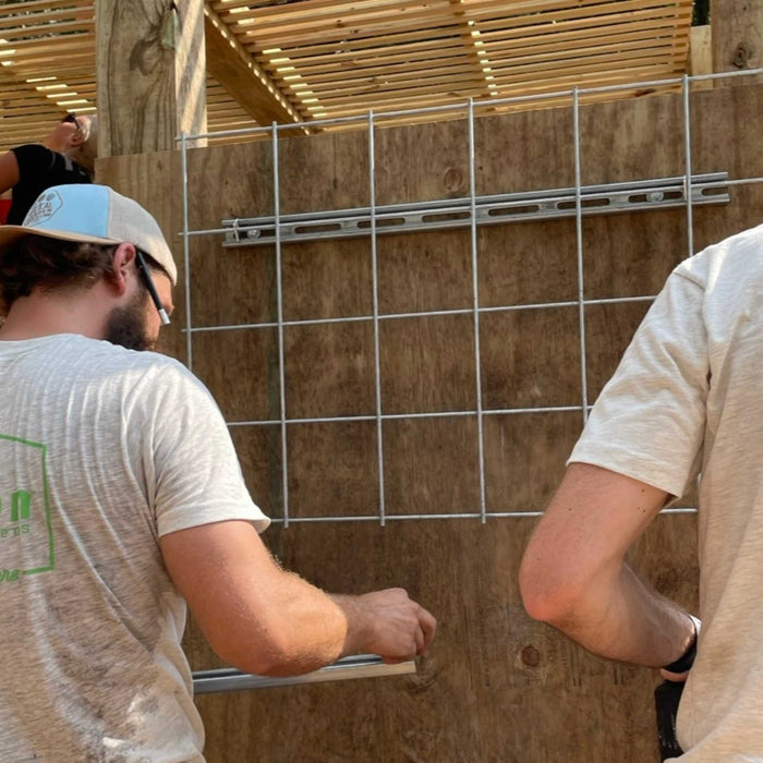 Workers installing metal grid and support channels on a wooden wall. Outdoor construction of a pergola and trellis.