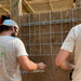 Workers installing metal grid and support channels on a wooden wall. Outdoor construction of a pergola and trellis.
