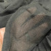 Hand behind sheer dark gray open-knit fabric, showcasing its transparent, breathable mesh texture.