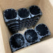 Black modular plastic plant pots with star-shaped bottoms, stacked in a cardboard box for hydroponic or aeroponic growing.
