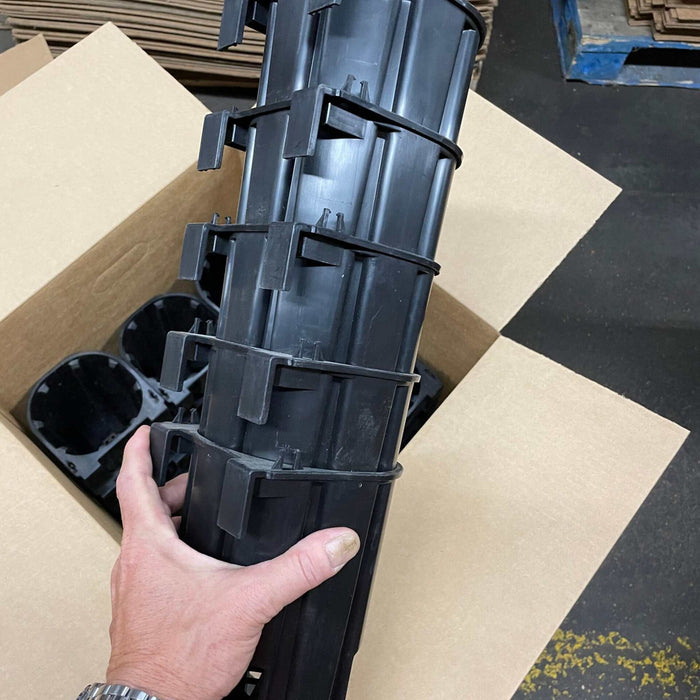 Hand holds stacked black plastic automotive components with clips, packing them in a box. Warehouse shipping.