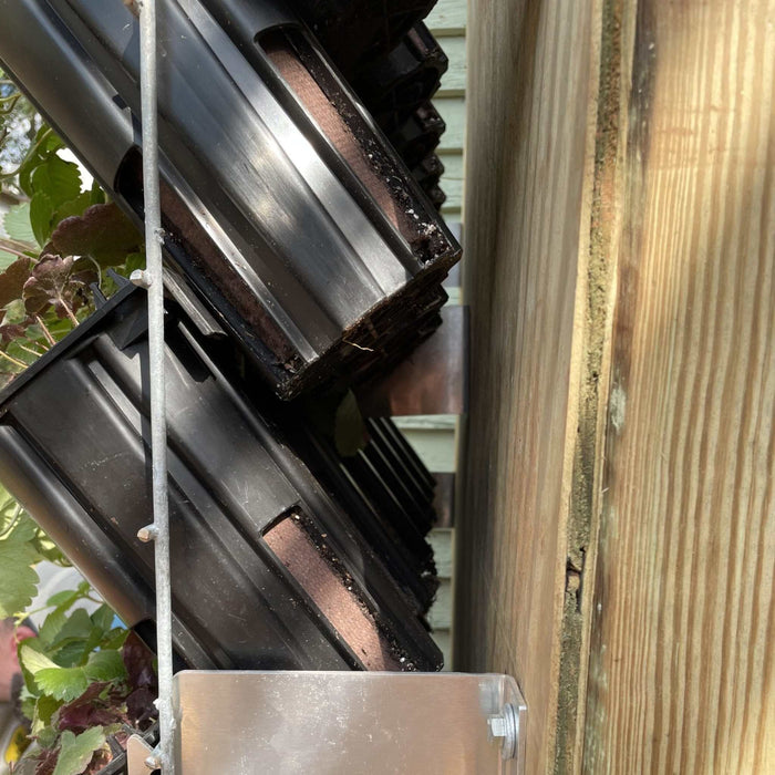 Black vertical garden planters with green plants mounted on a wood fence. Space-saving modular wall garden system.
