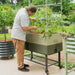 Man tending tomato plants in a mobile green self-watering raised garden bed with integrated trellis. Backyard gardening.
