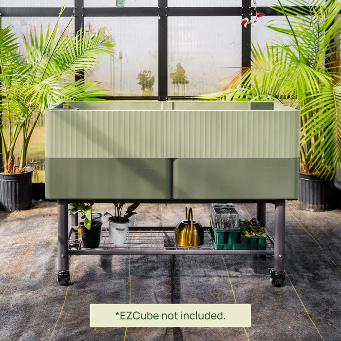 Vego Garden two-tone green mobile raised garden bed on wheels. Shelf with potted plants, golden watering can, seed trays in greenhouse.