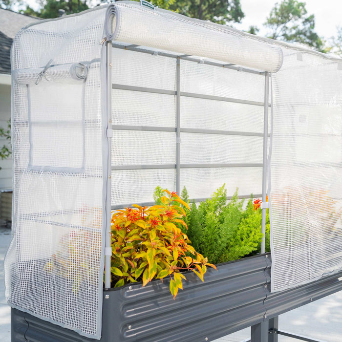 Corrugated metal raised garden bed with a white mesh greenhouse cover. Rolled-up side panels reveal colorful plants.