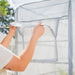 Hands opening clear, gridded mini greenhouse flap for ventilation. Great for plant protection, seed starting, and outdoor gardening.