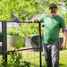 Smiling man next to a black metal garden trellis with young grapevines. Raised garden beds in a sunny backyard.