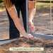Gardener assembling gray metal garden trellis with twine netting in a raised garden bed.
