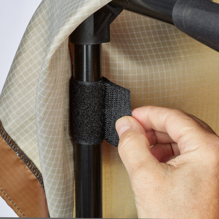Hand securing beige ripstop fabric to a black tent pole with a hook-and-loop strap. Camping gear assembly.