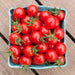 Ripe, vibrant red cherry tomatoes with green stems in a blue berry basket on a rustic wooden table.