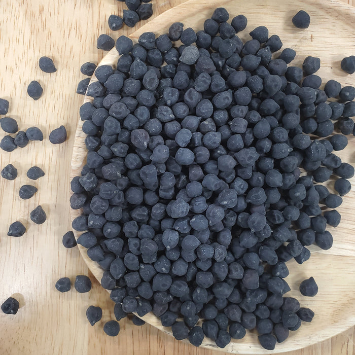 Black chickpeas (Kala Chana) piled on a wooden plate. Nutrient-rich, protein-packed legumes for healthy cooking.