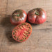 Two whole, one sliced dark red heirloom beefsteak tomatoes on rustic wood. Fresh garden produce.