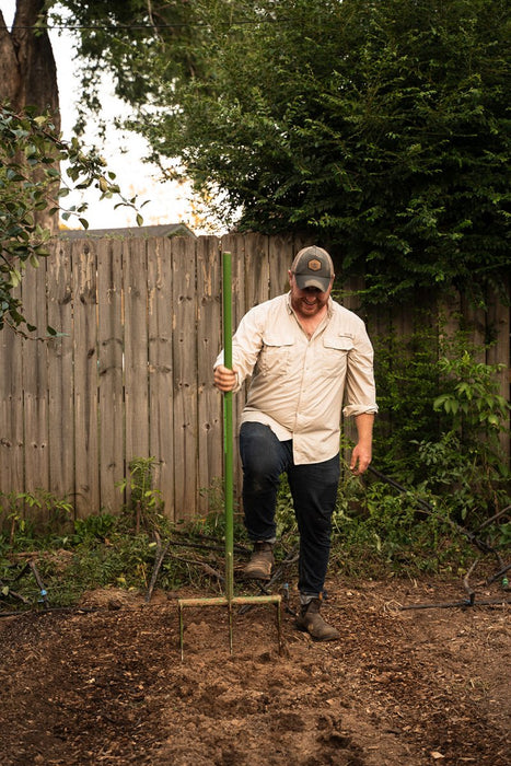 Gardener using broadfork to loosen and aerate soil in backyard garden, preparing for planting.