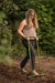 Woman using green "Mindful Farmer" garden tool to cultivate soil. Lush outdoor garden background.