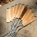 Several copper plant tags with metal loops and stakes, fanned on a textured concrete surface. Reusable garden markers.