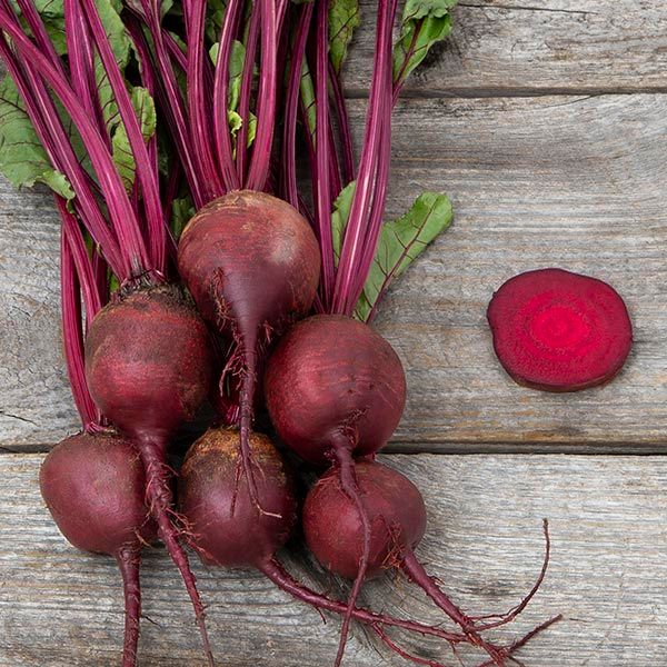 Fresh beets with vibrant red stems, green leaves, and a sliced beet on rustic wood. Healthy root vegetables.