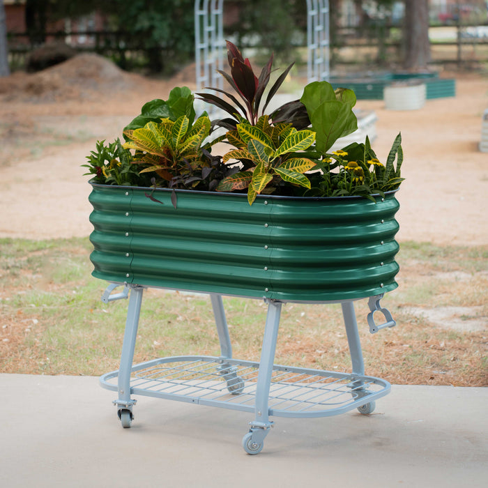 Green corrugated steel mobile raised garden bed on wheels with diverse plants. Features lower shelf and handle. Ideal patio planter.