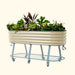 Corrugated beige metal mobile raised garden bed on grey wheeled stand with storage shelf, filled with vibrant plants & flowers.