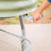 Hand holds lever on sage green mobile raised planter with wheels and bottom shelf for outdoor gardening.