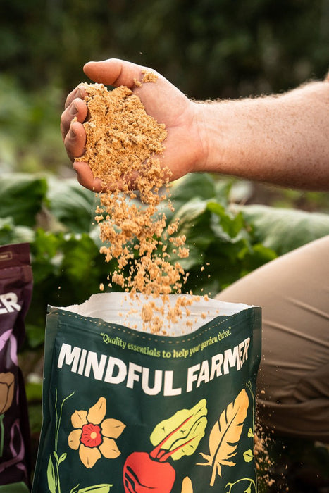 Hand pouring Mindful Farmer granular garden fertilizer into a bag. Organic soil amendment for healthy plants and thriving gardens.
