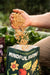 Hand pouring Mindful Farmer granular garden fertilizer into a bag. Organic soil amendment for healthy plants and thriving gardens.