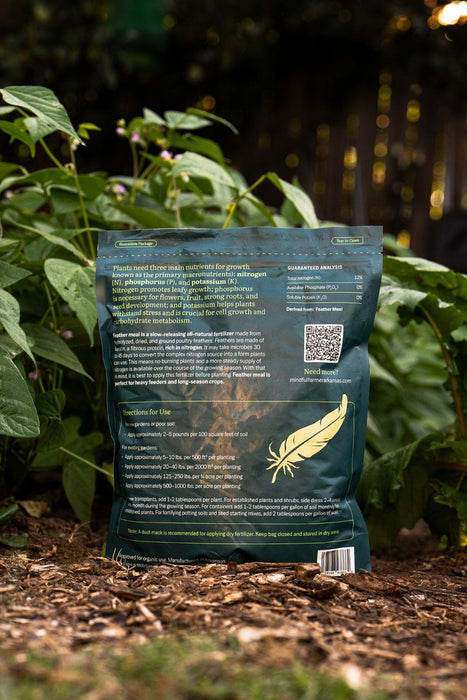 Organic Feather Meal fertilizer bag with nutrient details and feather logo, standing in a lush garden bed.