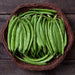 Fresh green beans in a woven basket on dark wood. Organic vegetables, healthy garden produce.