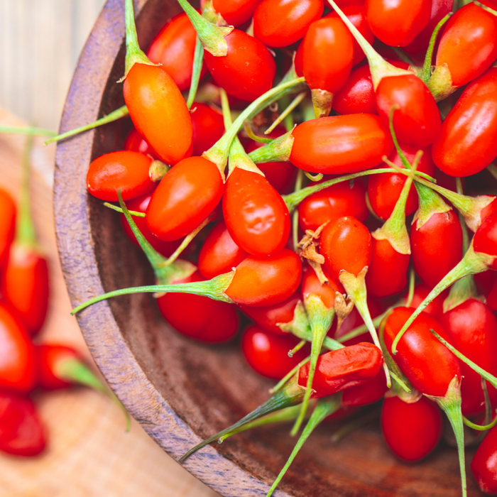 Close-up of fresh, bright red goji berries with green stems in a rustic wooden bowl. Healthy superfood fruit.