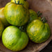 Fresh green and yellow striped heirloom tomatoes in a rustic wooden bowl.