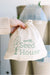 Hand holds GreenStalk garden "Seed House" drawstring bag with plant logo. Blurred vertical garden planter background.