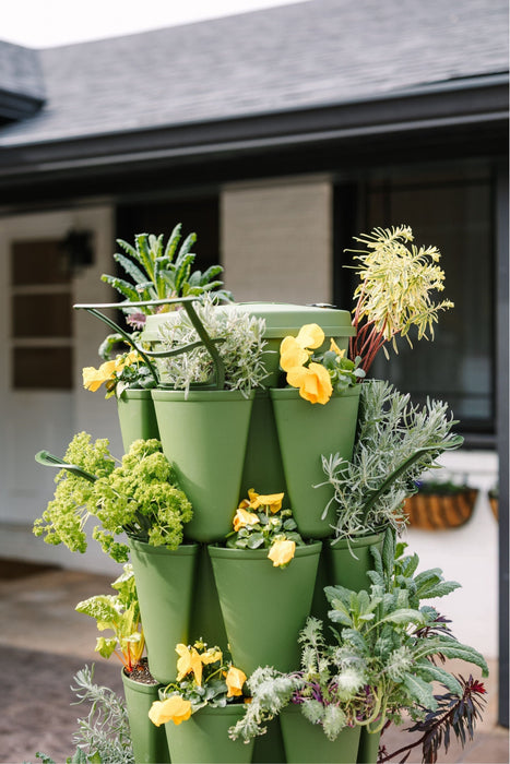 Green stackable vertical garden with lush herbs, kale, and yellow flowers growing outdoors.