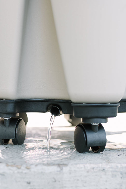 Light grey mobile vertical garden planter with water draining from its spout. Features casters for easy movement and efficient drainage.