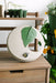 Decorative garden plate with green leaf, bee, and cutout on wood table. Seedlings, watering can, potted herbs.