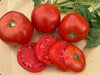 Ripe red tomatoes, whole and freshly sliced, on a wooden cutting board with green leaves. Fresh garden produce.